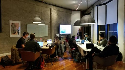 Diverse team collaborating in a modern office setting with laptops and presentation screen.