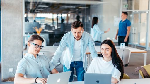 a group of people sitting around a table with laptops
