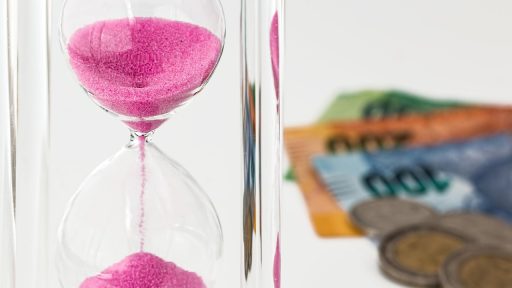 Munten naast een zandloper als symbool voor spaargeld dat in waarde daalt door de tijd